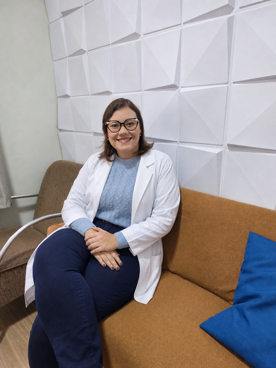 Dra Ana Carolina Oliveira sentada em consultório usando jaleco